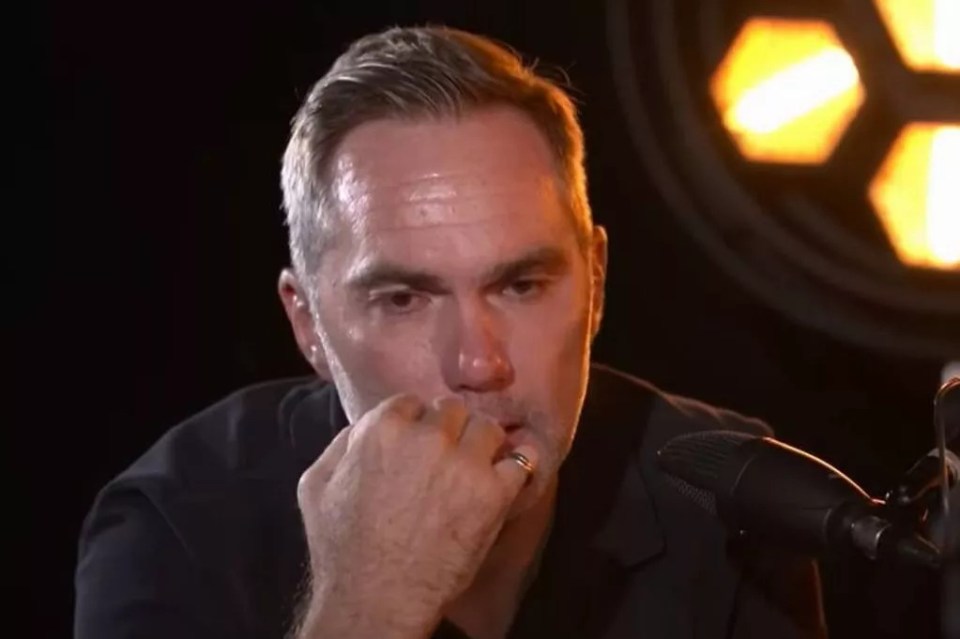 A man sits in front of a microphone, looking thoughtful.