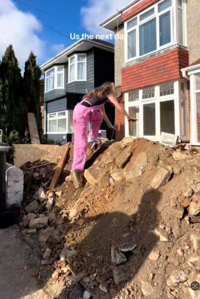 Woman in pink overalls removing debris from a house renovation.