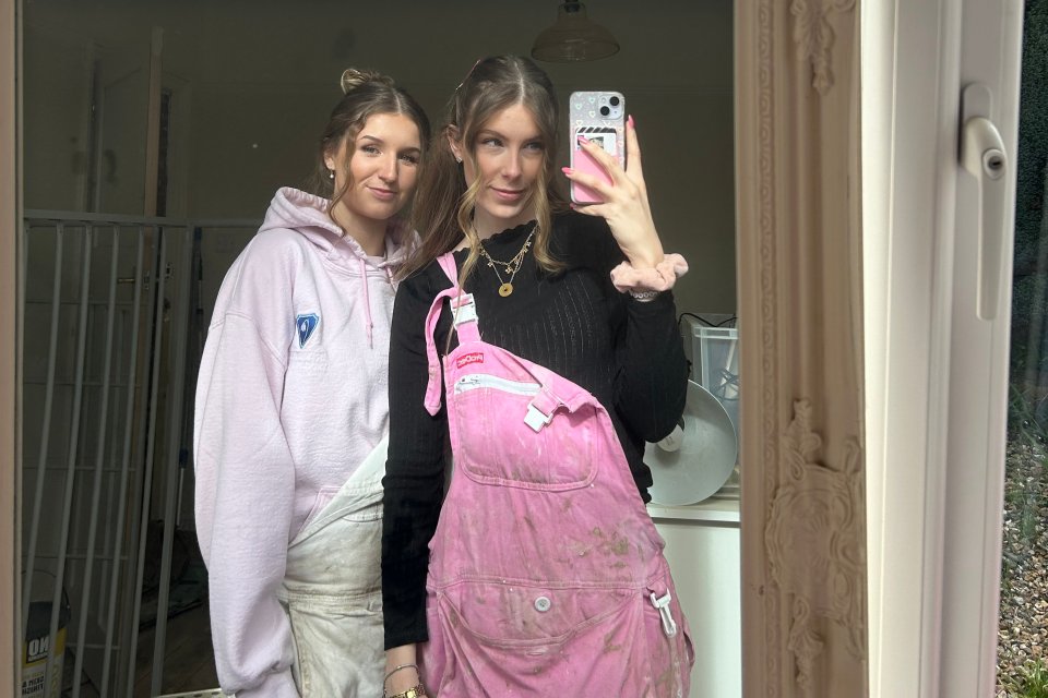 Two sisters in pink overalls taking a selfie during a home renovation.