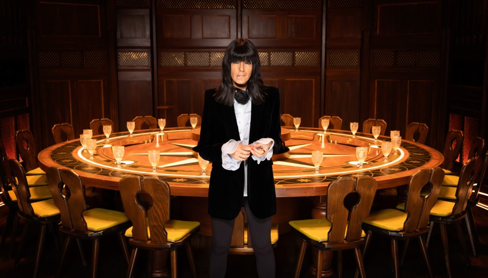 Claudia Winkleman standing behind a large round table.