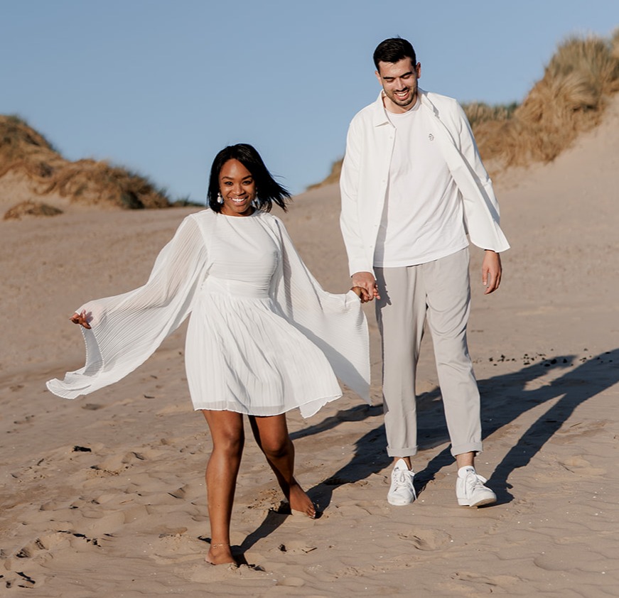 Couple holding hands and walking on a sandy beach.