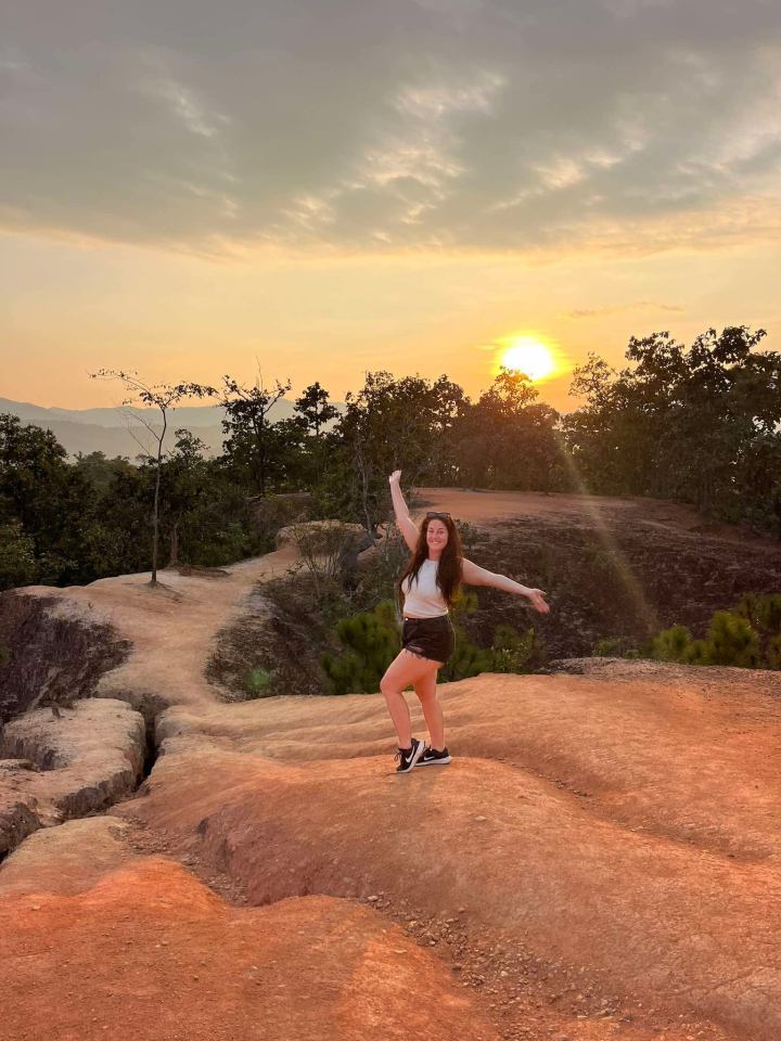 Woman standing on a red rock formation at sunset.