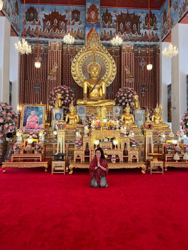 Woman praying in front of a golden Buddha statue in a Thai temple.