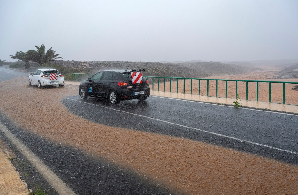 Cars driving on a flooded road during a heavy rainstorm.