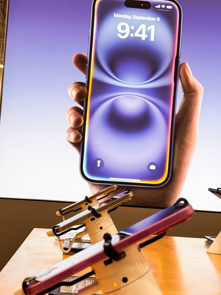 A hand holding a large iPhone, with several other iPhones on display in the foreground.