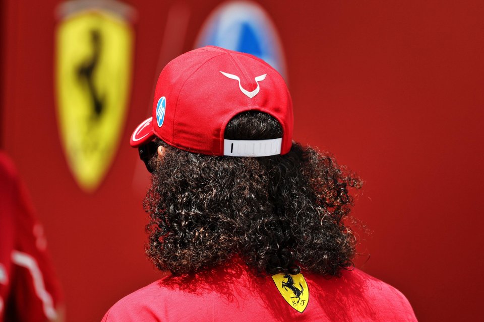 Back of a person's head with long curly hair, wearing a red Ferrari hat.