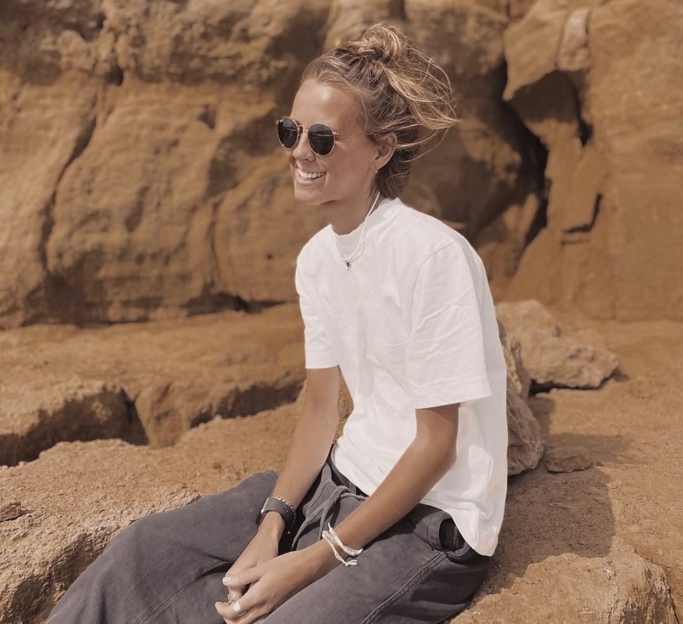 Woman sitting on rocks wearing sunglasses and a white t-shirt.