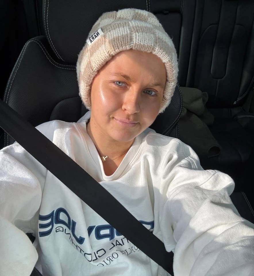 Woman with shaved head wearing a beanie and sweatshirt in a car.