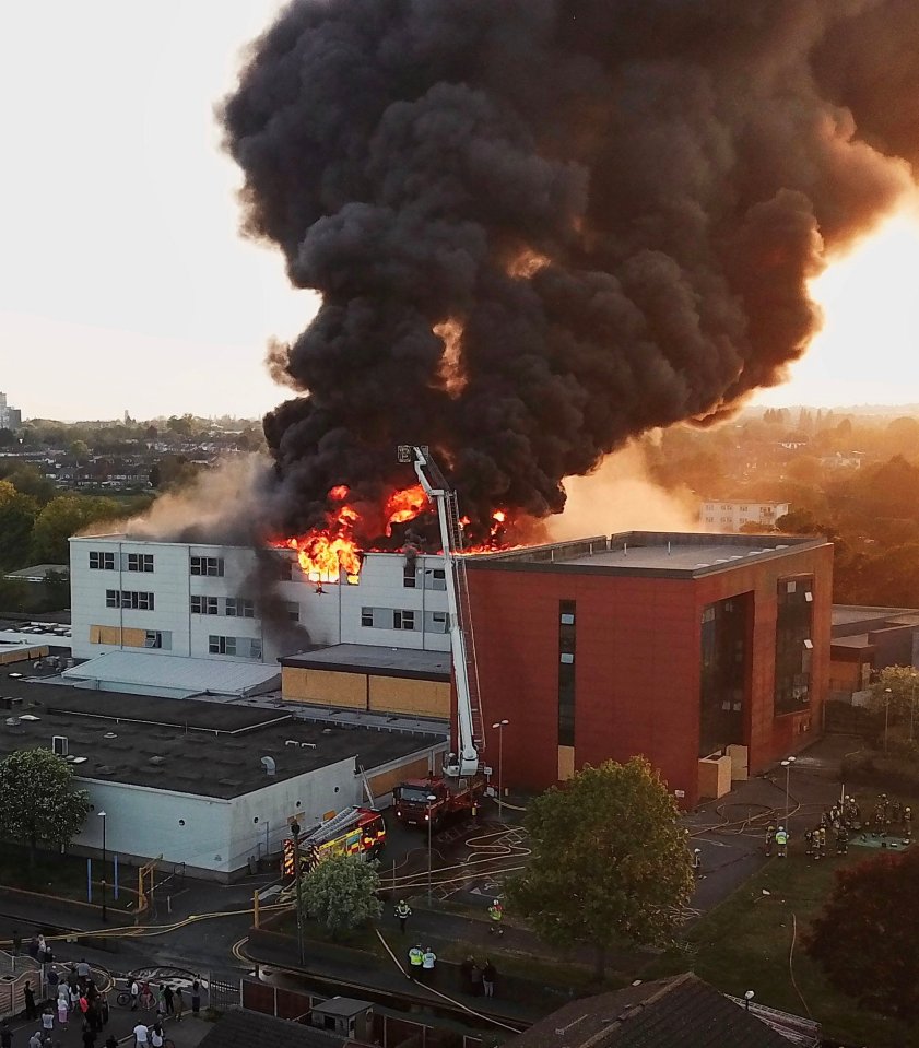 Aerial view of a large fire engulfing a building, with firefighters on the scene.