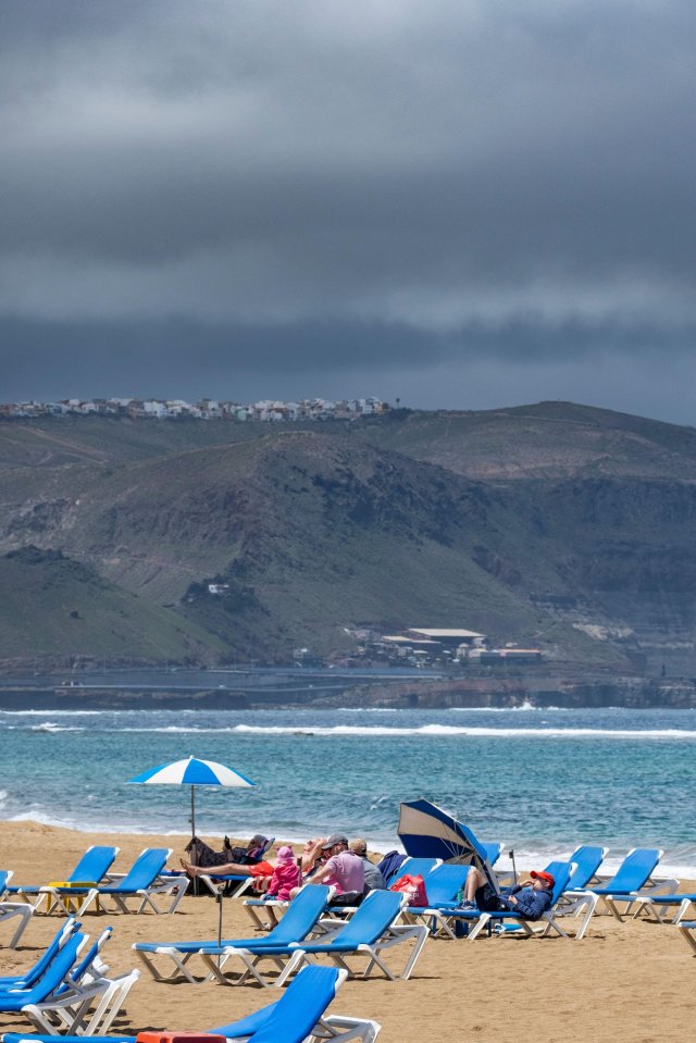 Tourists relaxing on a beach in Las Palmas as rain clouds gather.