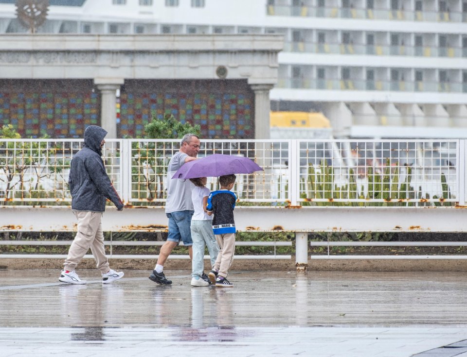 Tourists sheltering under an umbrella near a cruise ship in the rain.