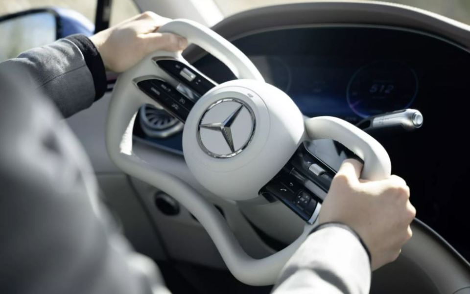 Person's hands on a white yoke-shaped steering wheel in a Mercedes-Benz.