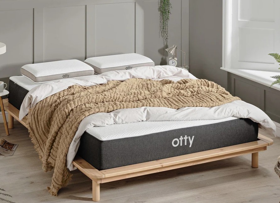 Otty Original Hybrid mattress on a wooden frame with pillows and blanket.