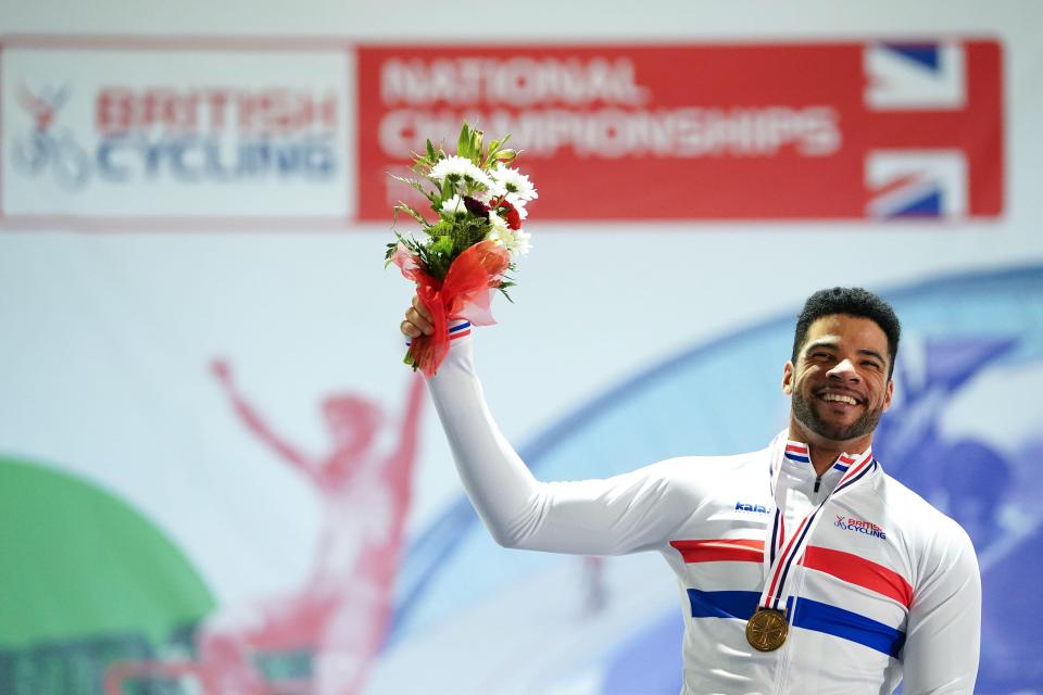 A cyclist holding a bouquet of flowers and a gold medal after winning a race.