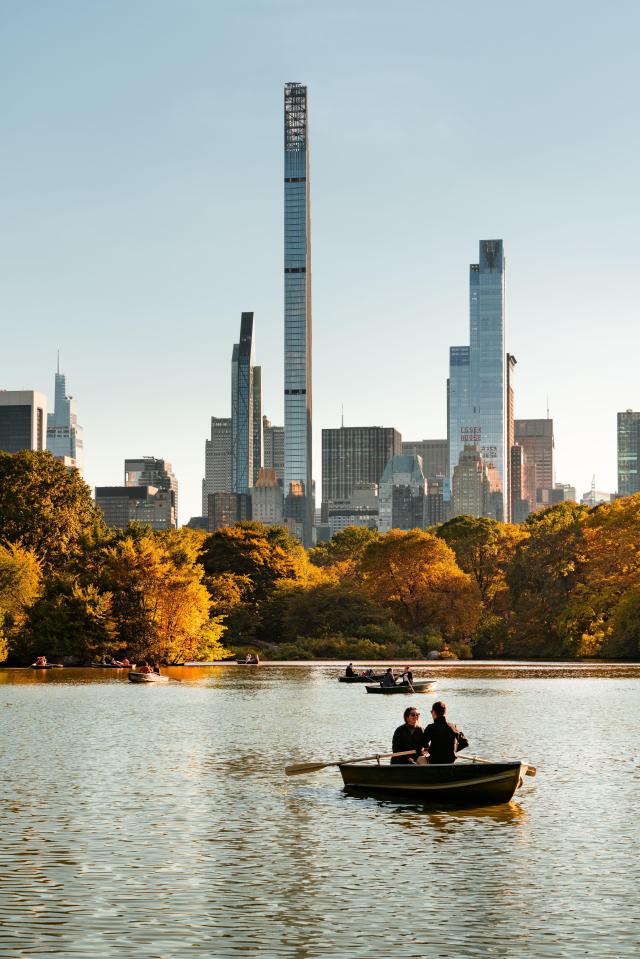 People boating on a lake in Central Park with Midtown Manhattan skyscrapers in the background.