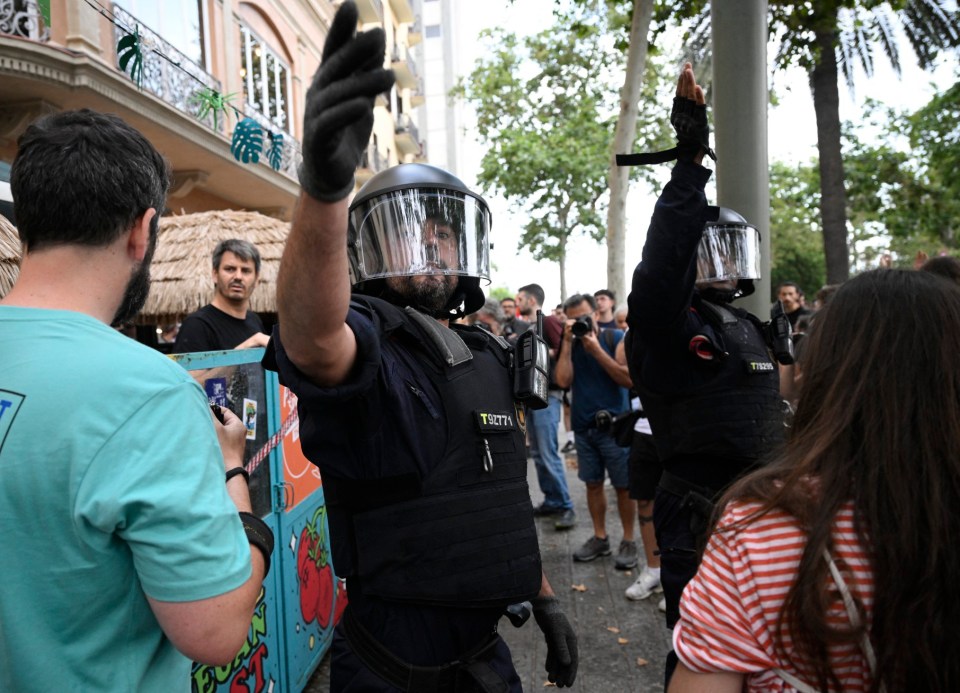 Anti-riot forces gestuer as demonstrators put symbolic cordon on a bar-restaurant window during a protest against mass tourism on Barcelona's Las Ramblas alley, on July 6, 2024. Protests against mass tourism have multiplied in recent months across Spain, the world's second-most visited country. (Photo by Josep LAGO / AFP) (Photo by JOSEP LAGO/AFP via Getty Images)
