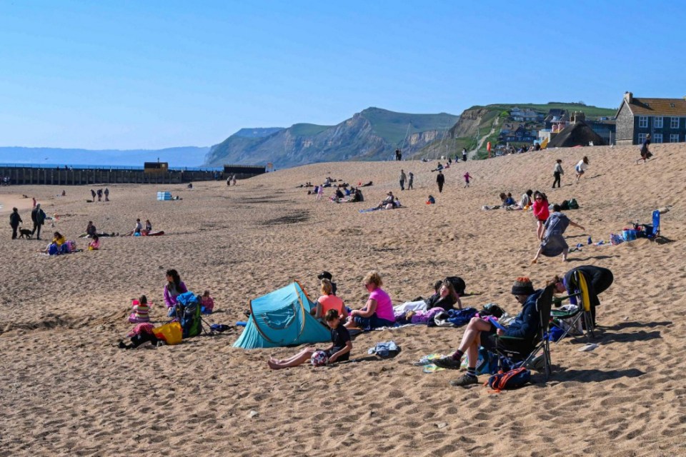 Alamy Live News. 3AFAHDK West Bay, Dorset, UK. 7th April 2025. UK Weather. Beachgoers enjoying the hot spring sunshine and clear blue skies at West Bay in Dorset during the Easter school holidays. Picture Credit: Graham Hunt/Alamy Live News This is an Alamy Live News image and may not be part of your current Alamy deal . If you are unsure, please contact our sales team to check.