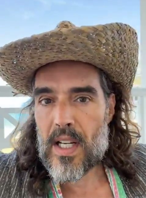 Close-up of a man with long hair and a beard wearing a straw hat, speaking.