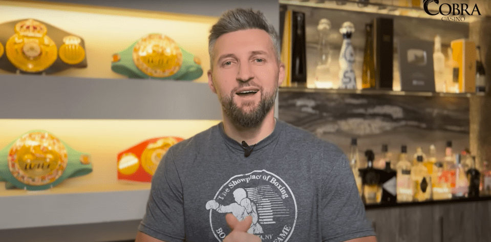 Man speaking in front of boxing belts and liquor bottles.