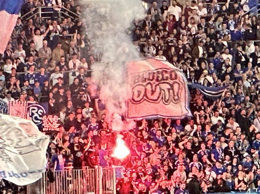 Crowd at a sporting event with a large banner and flares.