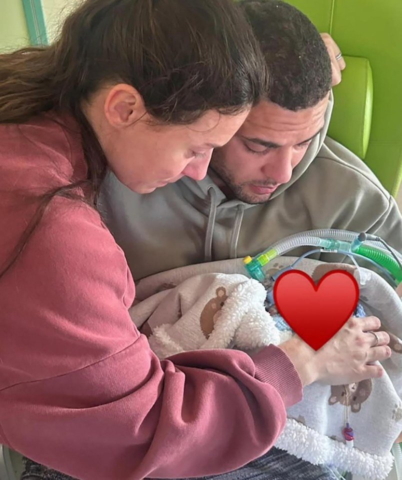 Parents holding their baby son who is connected to medical equipment.