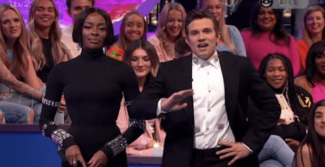 Two hosts standing in front of a studio audience.
