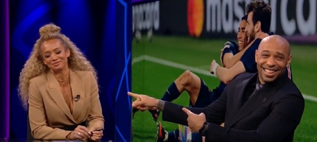 A woman and two men on a sports show; one man points to a soccer game playing on a screen.