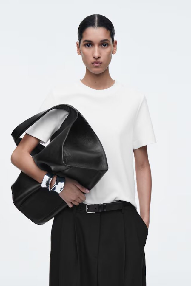 Woman wearing a white t-shirt, black pants, and a black tote bag.