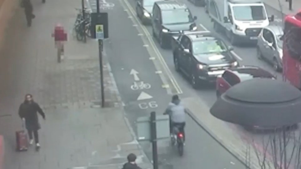 A cyclist riding in a bike lane alongside a street with pedestrians and cars.