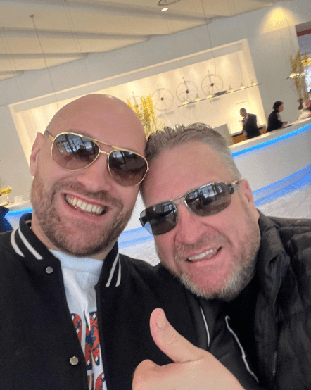 Selfie of two men wearing sunglasses, one giving a thumbs up.