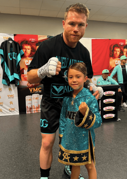 A boxer poses with a young girl wearing a boxing robe.