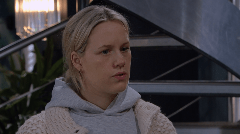 Screenshot of a blonde woman wearing a gray hoodie and a cream cardigan.