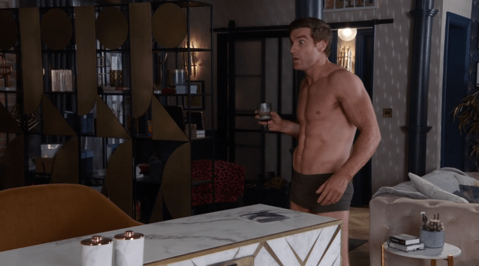 Shirtless man holding a drink in a stylish apartment.