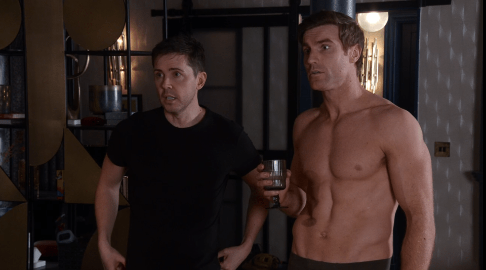 Screenshot of two men, one shirtless, the other in a black t-shirt, one holding a glass.