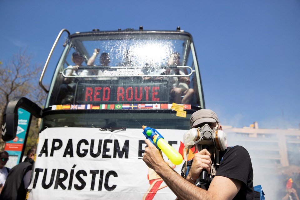 Protestors blocking a tourist bus with a banner reading "Lets turn off the tourist fire".