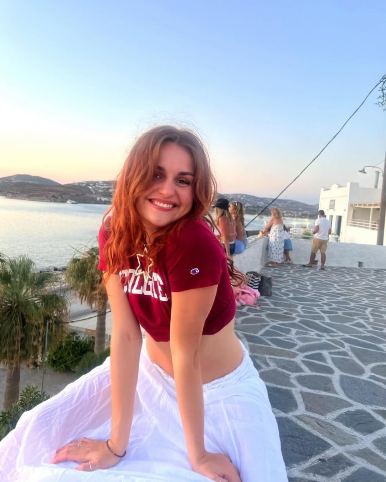 Alexandra Vladimirov of AU Strictly sitting on a stone wall overlooking the ocean.