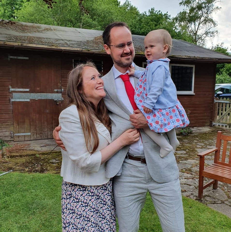 Family portrait: a man and woman embracing, holding their toddler daughter.