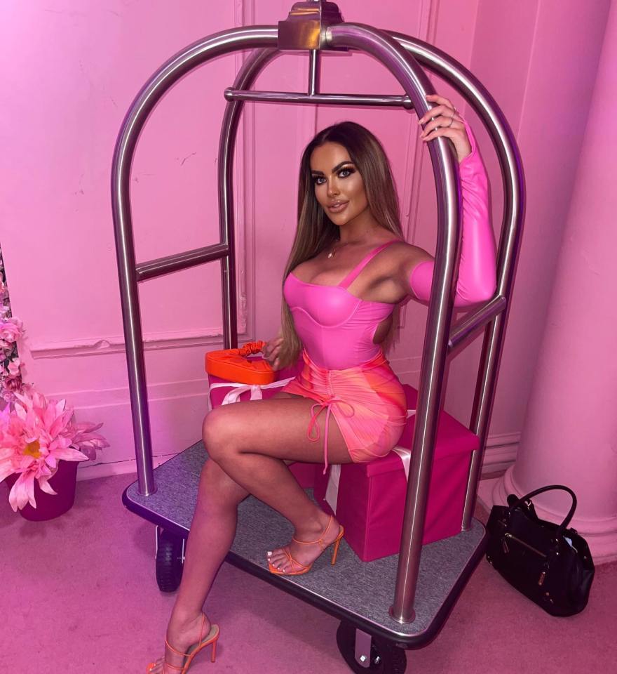 Woman in pink dress sitting on luggage cart.