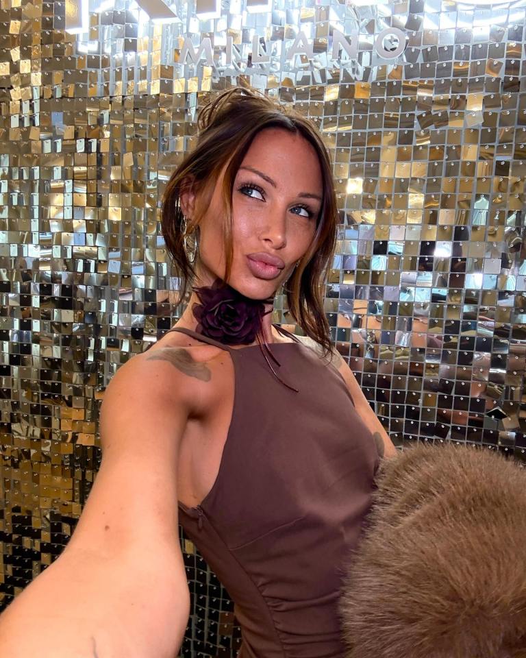 Woman in brown dress taking selfie in front of a mirrored wall.