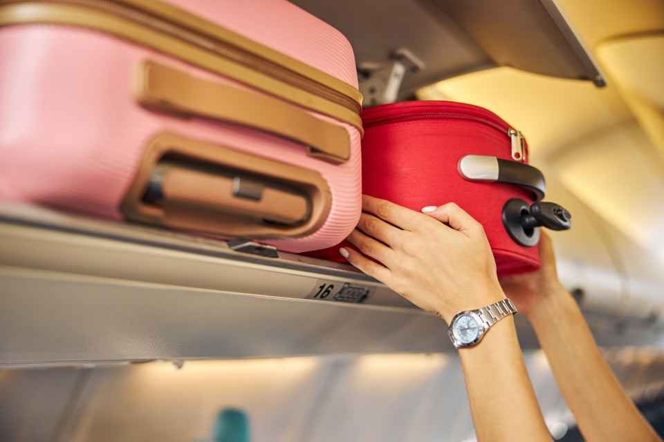 Woman placing carry-on luggage in overhead bin on airplane.
