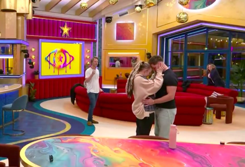 Celebrity Big Brother housemates embracing in the brightly colored living room.