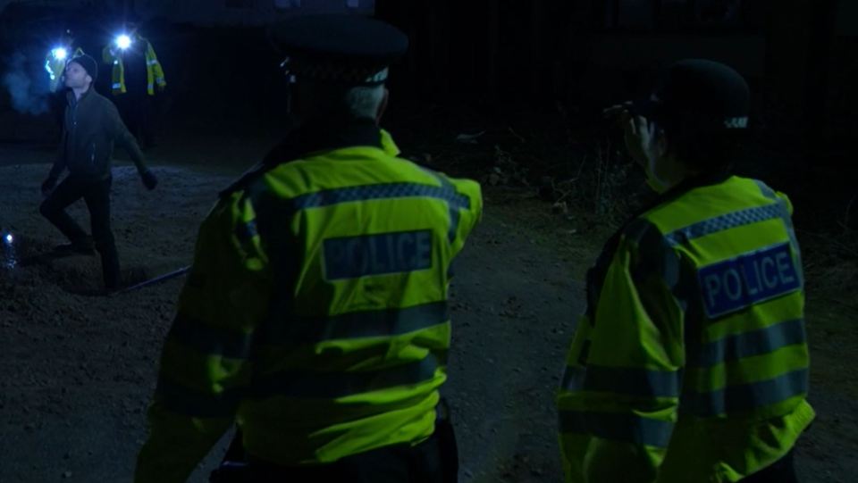 Police officers at night investigating a scene.