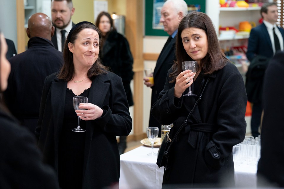Two women in black coats holding wine glasses at a gathering.