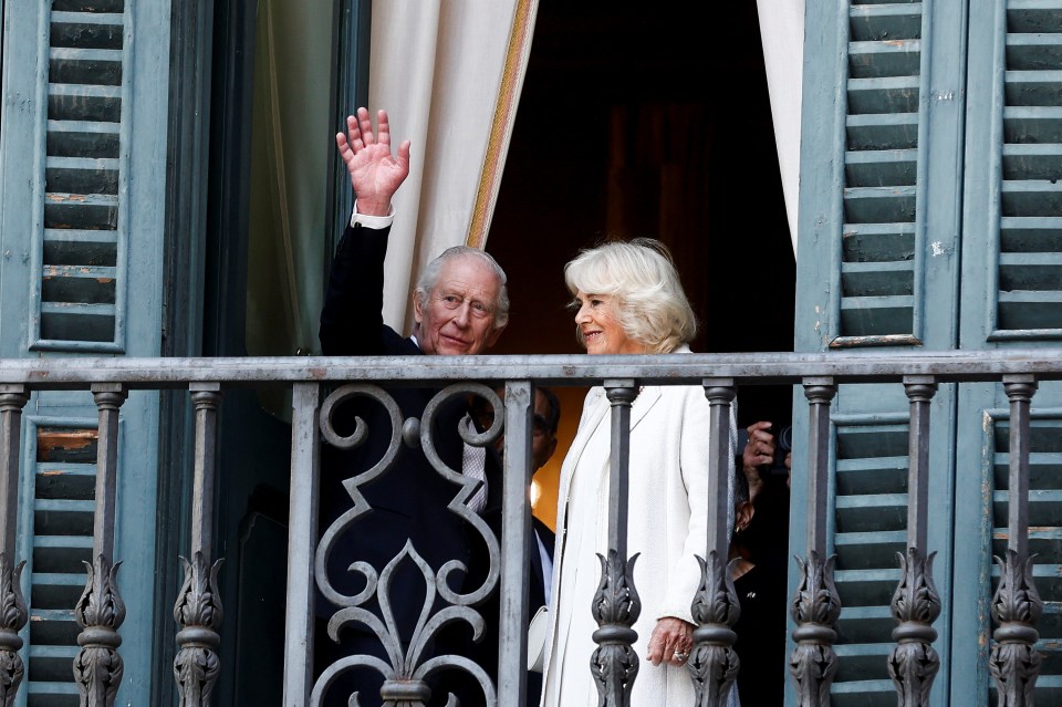 King Charles and Queen Camilla on a balcony, waving.