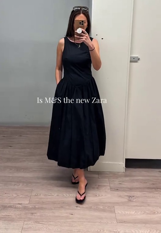 Woman in a black midi dress taking a selfie in a changing room.