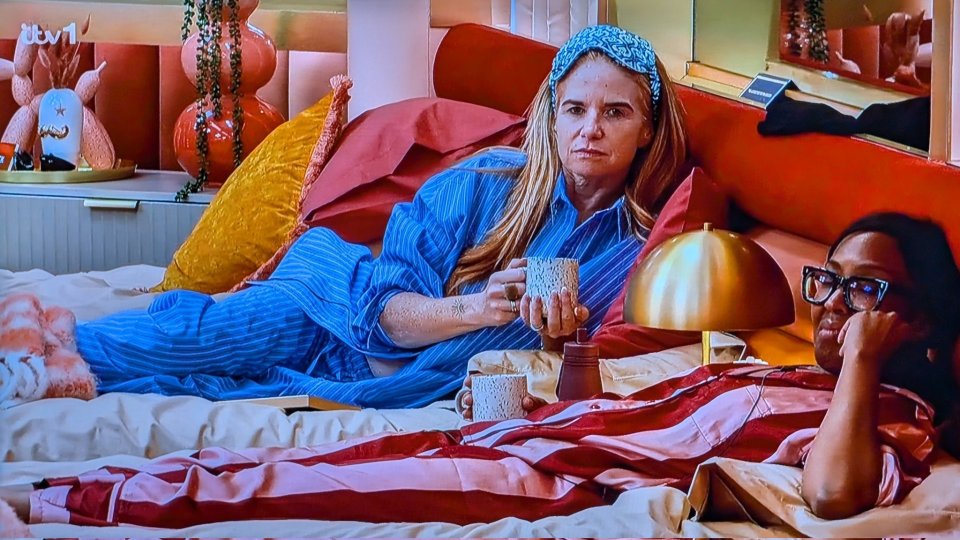 Two women in pajamas in bed, one holding a mug.