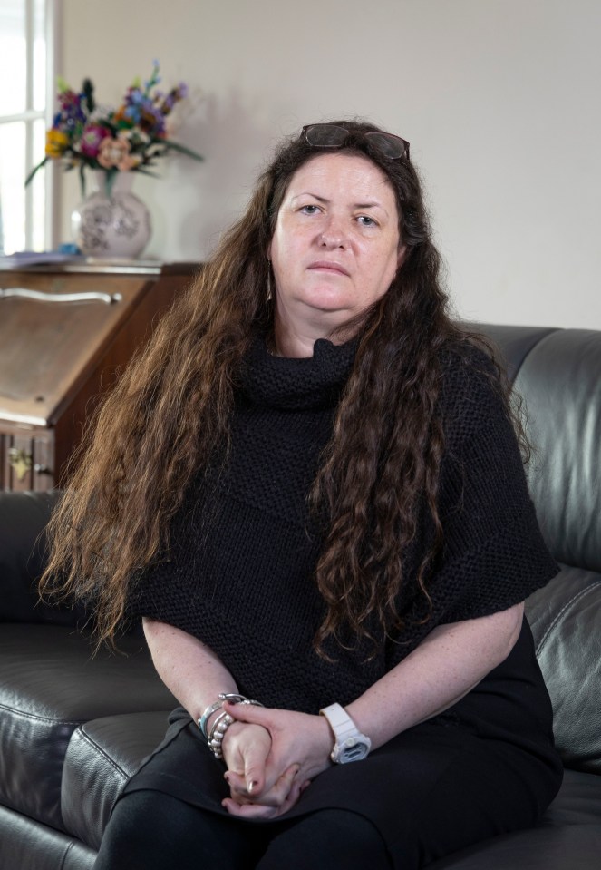 A woman with long brown hair sits on a couch, looking at the camera.