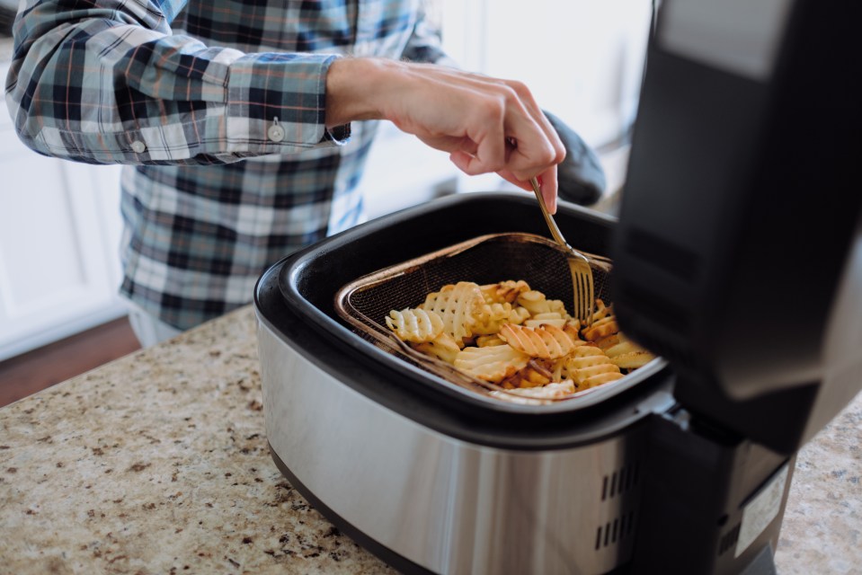 A man using a fork to check waffle fries cooking in an air fryer.