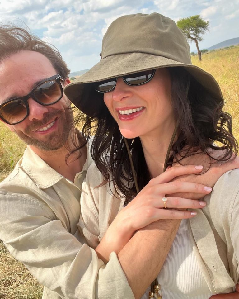 Couple embracing outdoors, woman showing engagement ring.