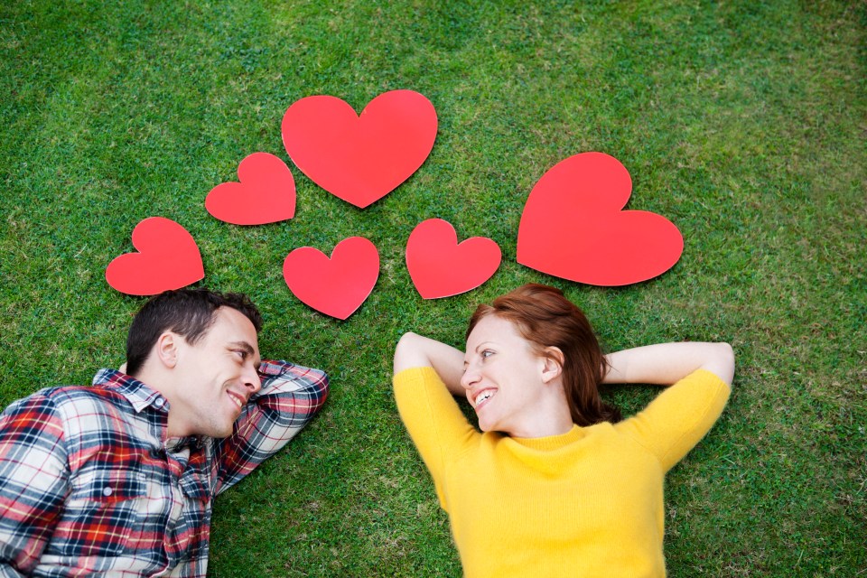 Couple lying on grass surrounded by red hearts.